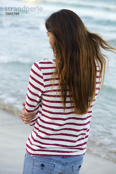 Junge Frau am Strand stehend  Rückansicht