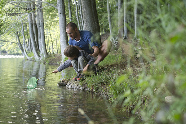 Vater und Sohn hocken am Ufer mit Fischernetz