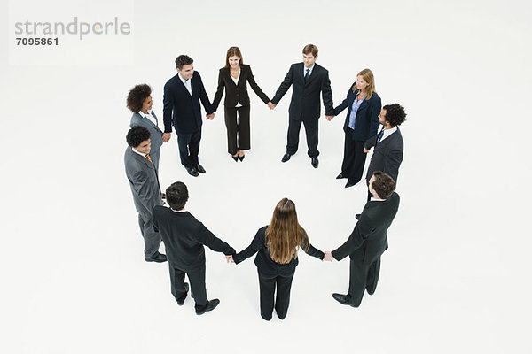 Geschäftsmänner und Geschäftsfrauen stehen im Kreis und halten Händchen.