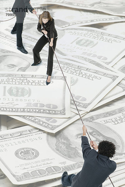 Executives spielen Tauziehen auf einem Haufen von Hundert-Dollar-Scheinen