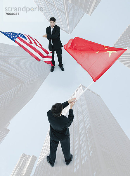 Geschäftsmann  der von Angesicht zu Angesicht steht und chinesische und amerikanische Flaggen schwenkt.