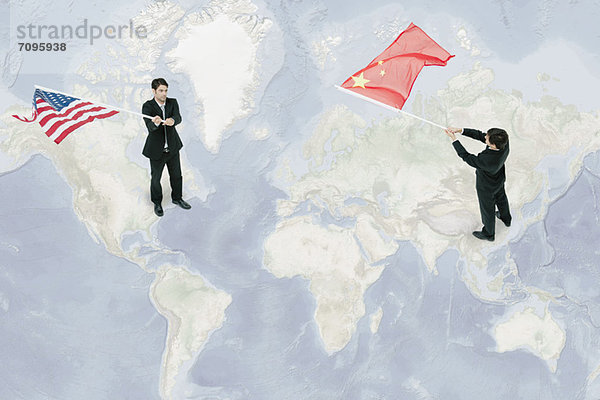 Geschäftsleute  die auf der Weltkarte stehen und amerikanische und chinesische Flaggen schwenken.