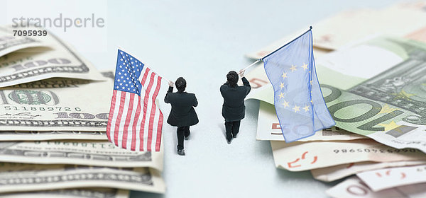 Geschäftsleute marschieren zwischen Geldhaufen und tragen amerikanische und europäische Flaggen.