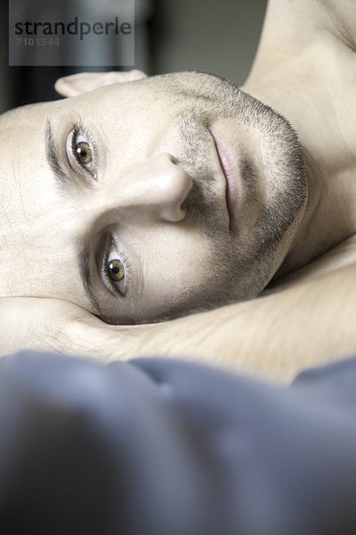 Mann mit Dreitagebart liegt im Bett  Portrait