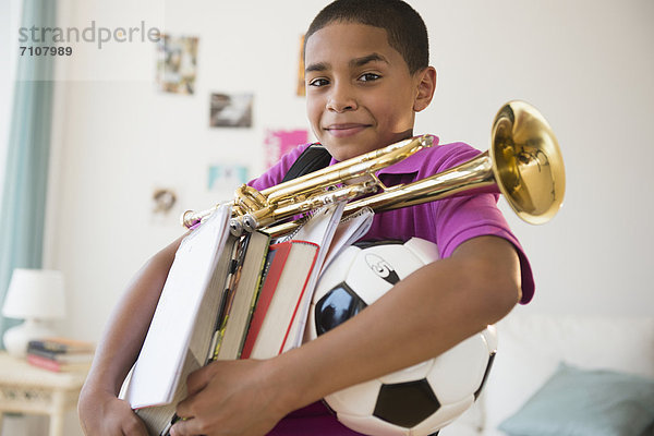 Hispanic boy carrying trumpet  books and soccer ball