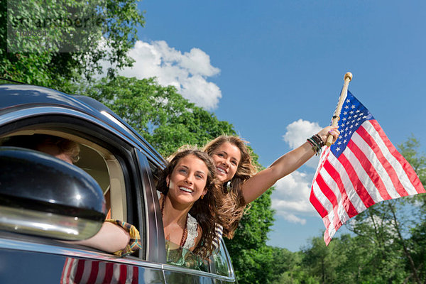 Zwei Freunde  die sich aus dem Autofenster lehnen und die amerikanische Flagge halten.