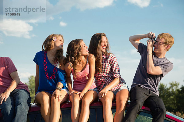 Freunde sitzen auf dem Autodach  junger Mann fotografiert