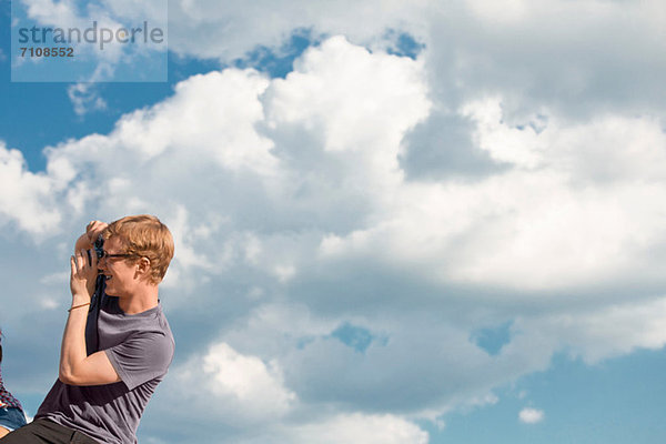 Junger Mann fotografiert mit Wolken am Himmel