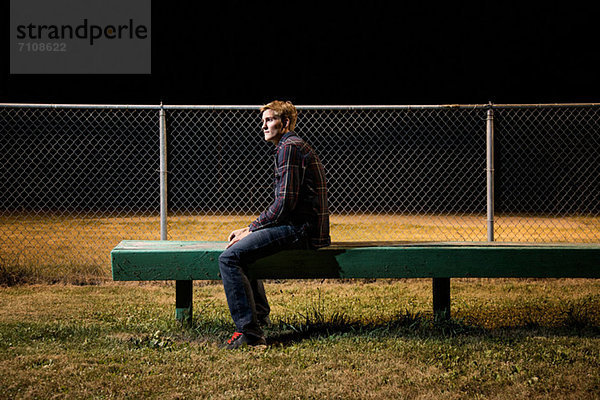 Nachdenklicher junger Mann  der nachts auf der Tribüne sitzt.