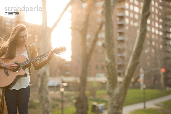 Junge Frau spielt Gitarre im Park