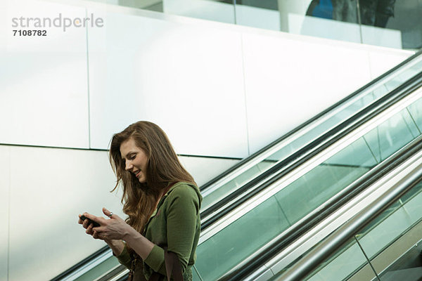 Junge Frau auf Rolltreppe mit Smartphone