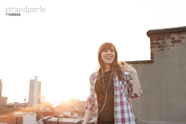 Junge Frau hört Musik auf dem Dach der Stadt