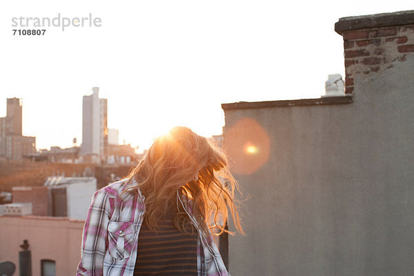 Junge Frau schüttelt Haare auf dem Stadtdach