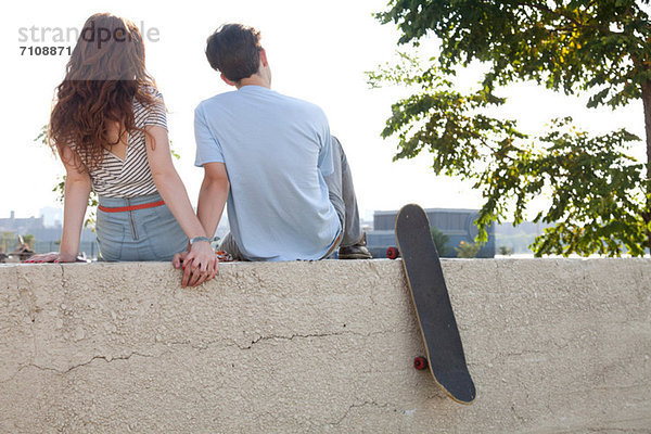 Junges Paar auf der Wand sitzend  Händchen haltend