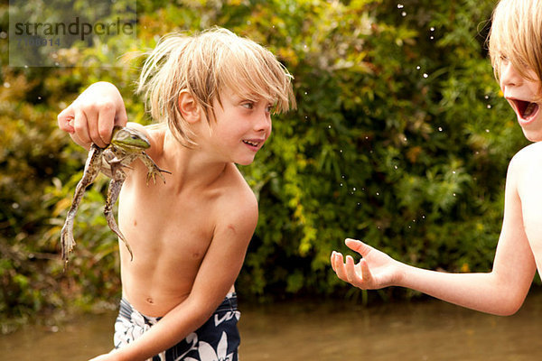 Junge hält Frosch hoch  während Freund staunend zusieht