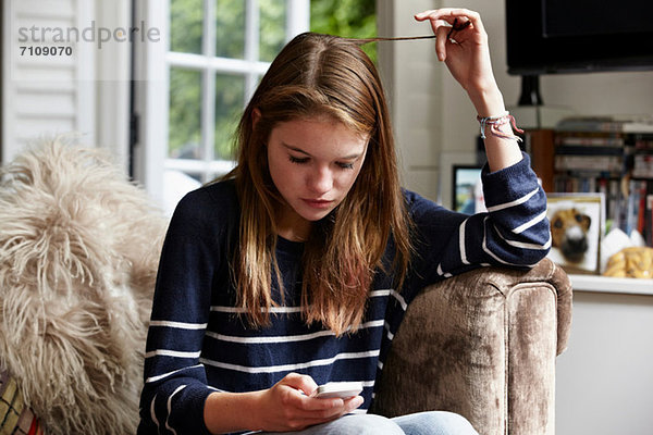Teenager schauen sich das Handy an und spielen mit ihren Haaren.