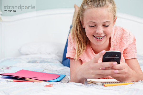 Teenager-Mädchen auf dem Bett liegend und mit Handy