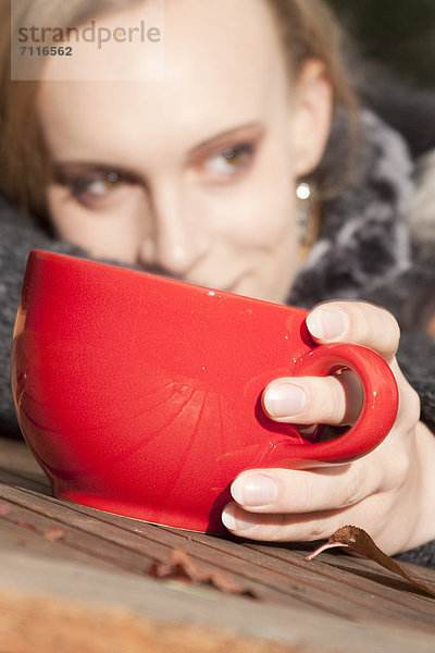 Blonde junge Frau mit einem Becher im Freien