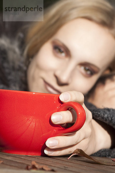 Blonde junge Frau mit einem Becher im Freien