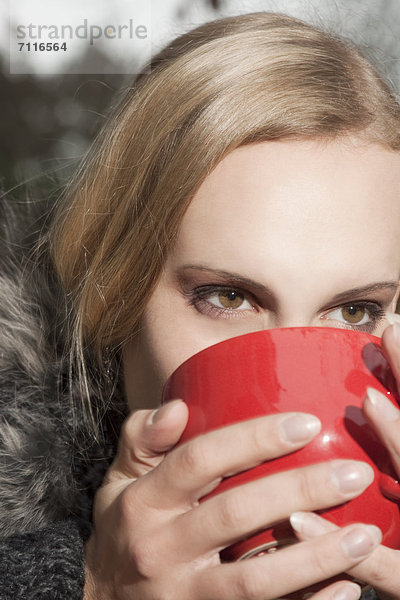 Blonde junge Frau trinkt aus einem Becher im Freien