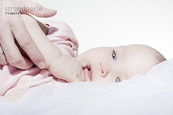 Hand eines Erwachsenen und Baby im Bett