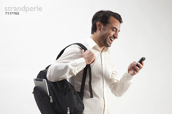 Lachender Mann mit Rucksack  aus dem ein iPad ragt  telefoniert mit dem Handy
