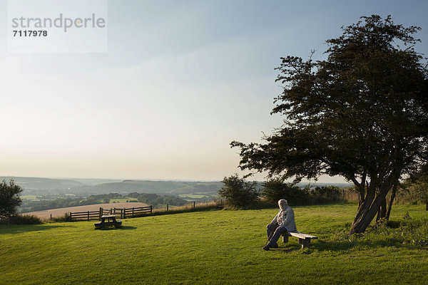 Ein älterer Mann sitzt auf einer Bank in einem Landschaftspark  Buriton  Hampshire  England  Großbritannien  Europa