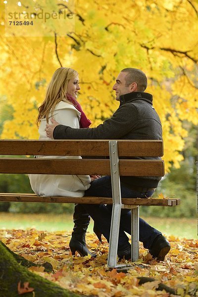 Paar sitzt auf einer Parkbank in herbstlicher Umgebung