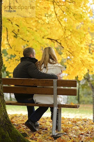 Paar sitzt auf einer Parkbank in herbstlicher Umgebung