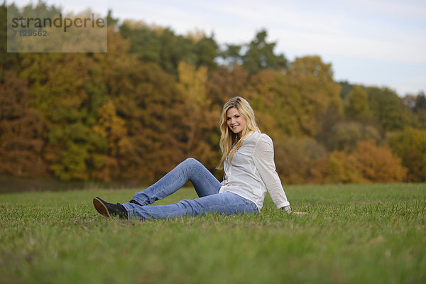 Lächelnde blonde junge Frau sitzt auf herbstlicher Wiese