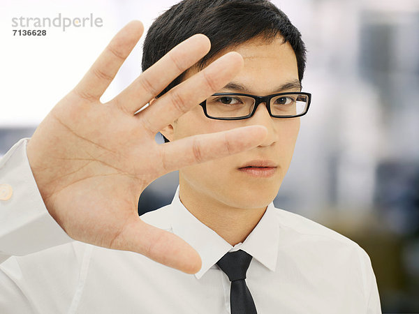 Junger Geschäftsmann  Asiate  mit Brille  hält Hand vor Gesicht  abweisend  ernst  gestresst