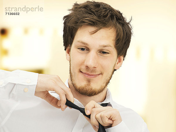 Portrait  junger Mann mit Bart  zieht Krawatte aus  lächelnd  entspannt