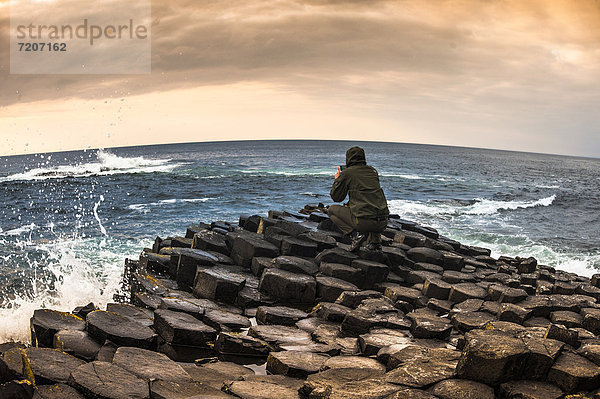 Mann fotografiert mit Smartphone  Basaltfelsen Giant's Causeway  Causeway Coast  Antrim  Nordirland  Großbritannien  Europa