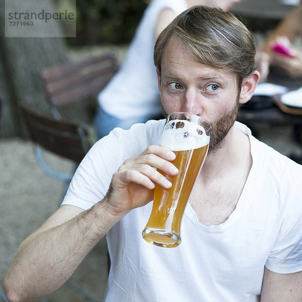 Mann trinkt Weißbier im Biergarten