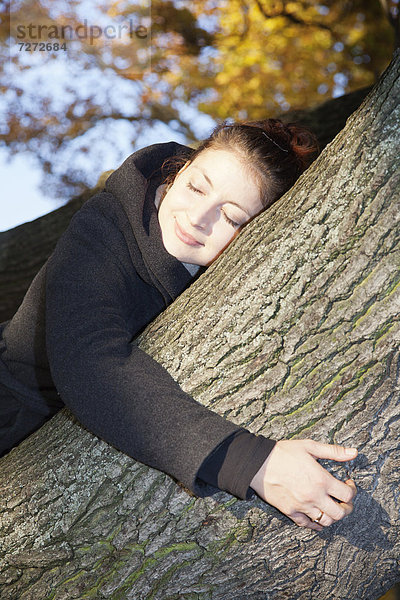 Junge Frau mit geschlossenen Augen auf einem Baum im Herbst