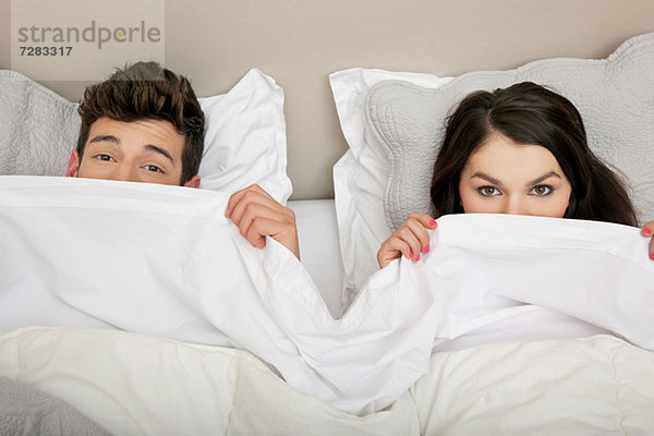Paar im Bett mit Blick hinter die Bettdecke