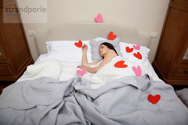 Frau schläft im Bett mit Herzformen auf der Bettwäsche