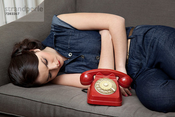 Frau auf Sofa liegend mit Telefon