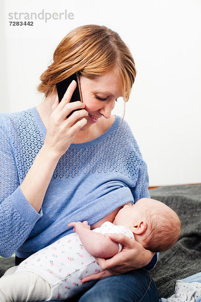 Mutter am Telefon stillende neugeborene Tochter