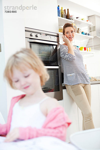 Mutter am Handy in der Küche mit Tochter im Vordergrund