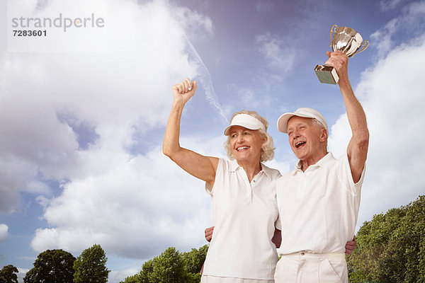 Seniorenpaar hält Tennistrophäe und Jubel