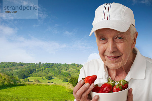 Älterer Mann in Tenniskleidung mit Erdbeeren gegen die ländliche Szene