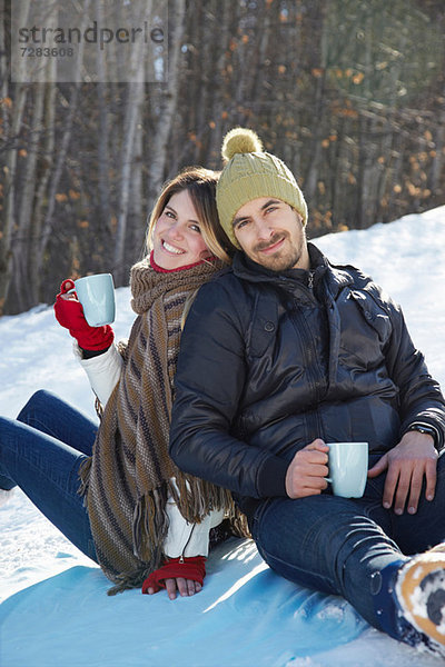 Porträt eines im Schnee sitzenden Paares mit heißen Getränken