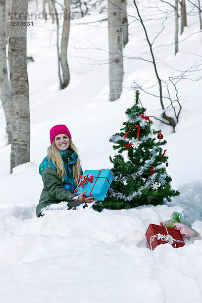 Frau sitzend am Weihnachtsbaum mit Geschenk