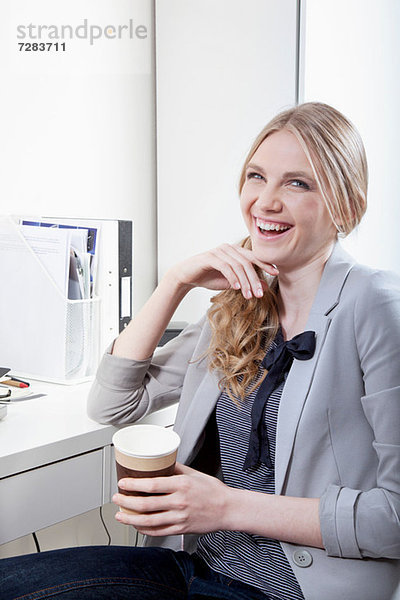 Glückliche junge Frau im Büro mit Kaffee