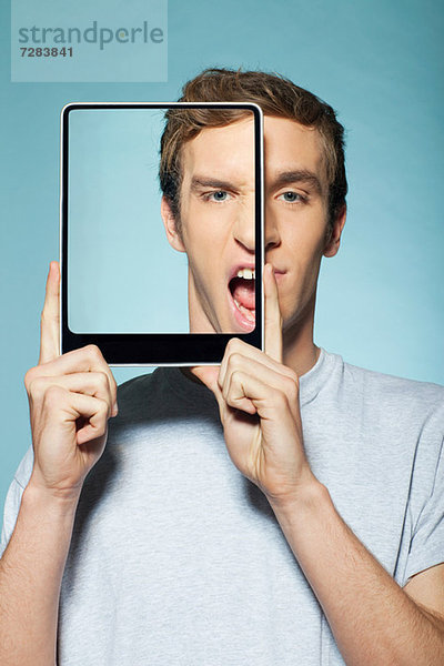 Mann  der sein halbes Gesicht mit einem digitalen Tablett bedeckt.