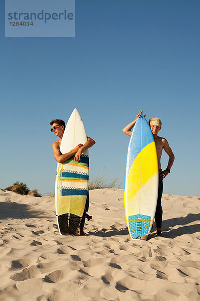 Zwei junge Männer stehen hinter Surfbrettern am Strand.