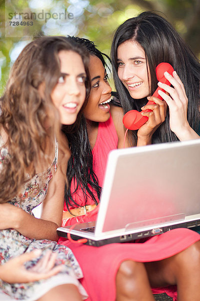 Frauen  die Laptop und Telefon benutzen  während sie auf einem Baumzweig sitzen.