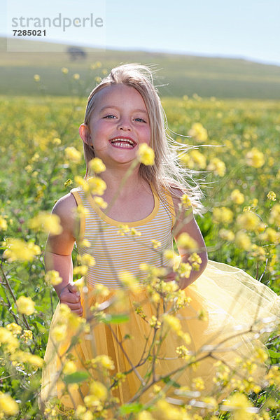 Lächelndes Mädchen spielt im Blumenfeld