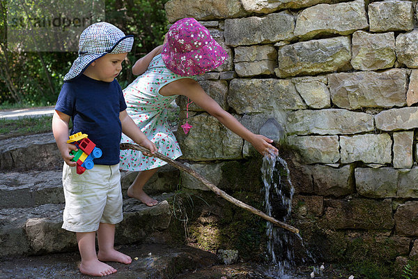 Kinder spielen am Wasserauslauf in der Wand